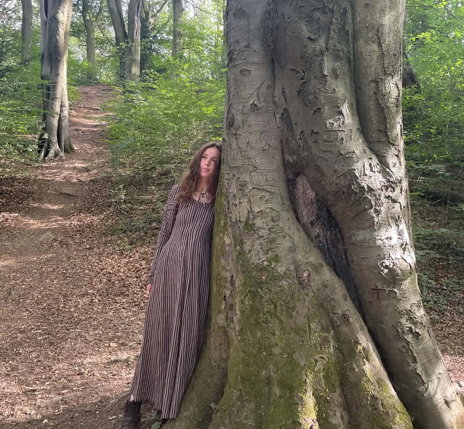 Jasmine leaning against a great beech tree on a woodland path, dappled light through the canopy