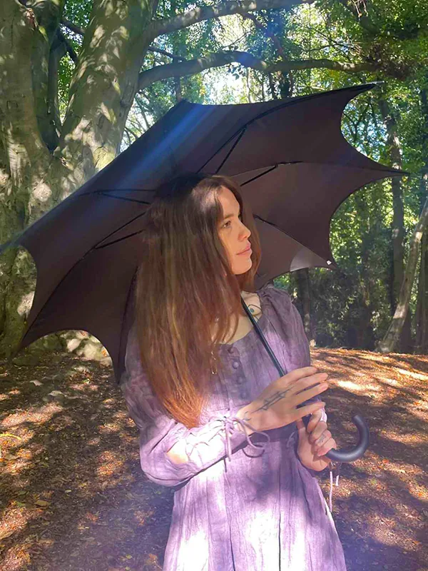 Jasmine holding a black umbrella in a sunlit wood