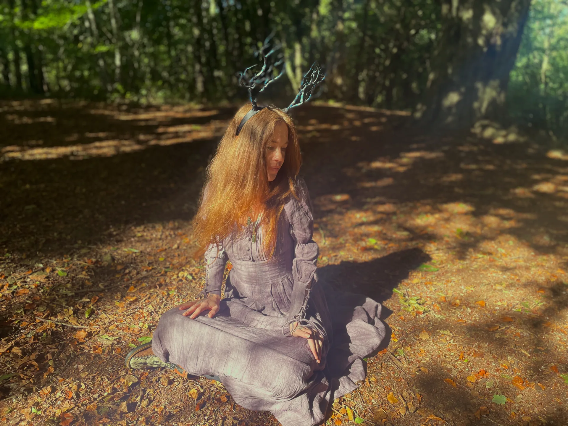 Jasmine seated on the forest floor in autumn light, wearing an antler headdress